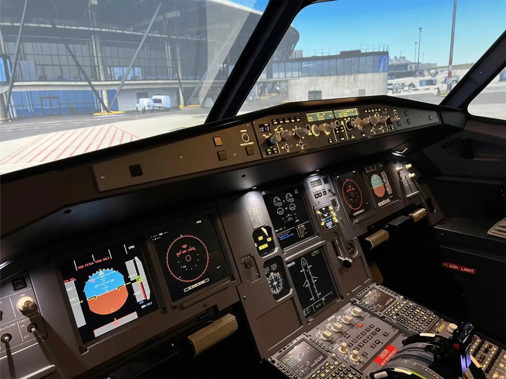 Vue rapprochée du tableau de bord d’un simulateur Airbus A320 montrant les instruments de vol et la scène extérieure de l’aéroport.