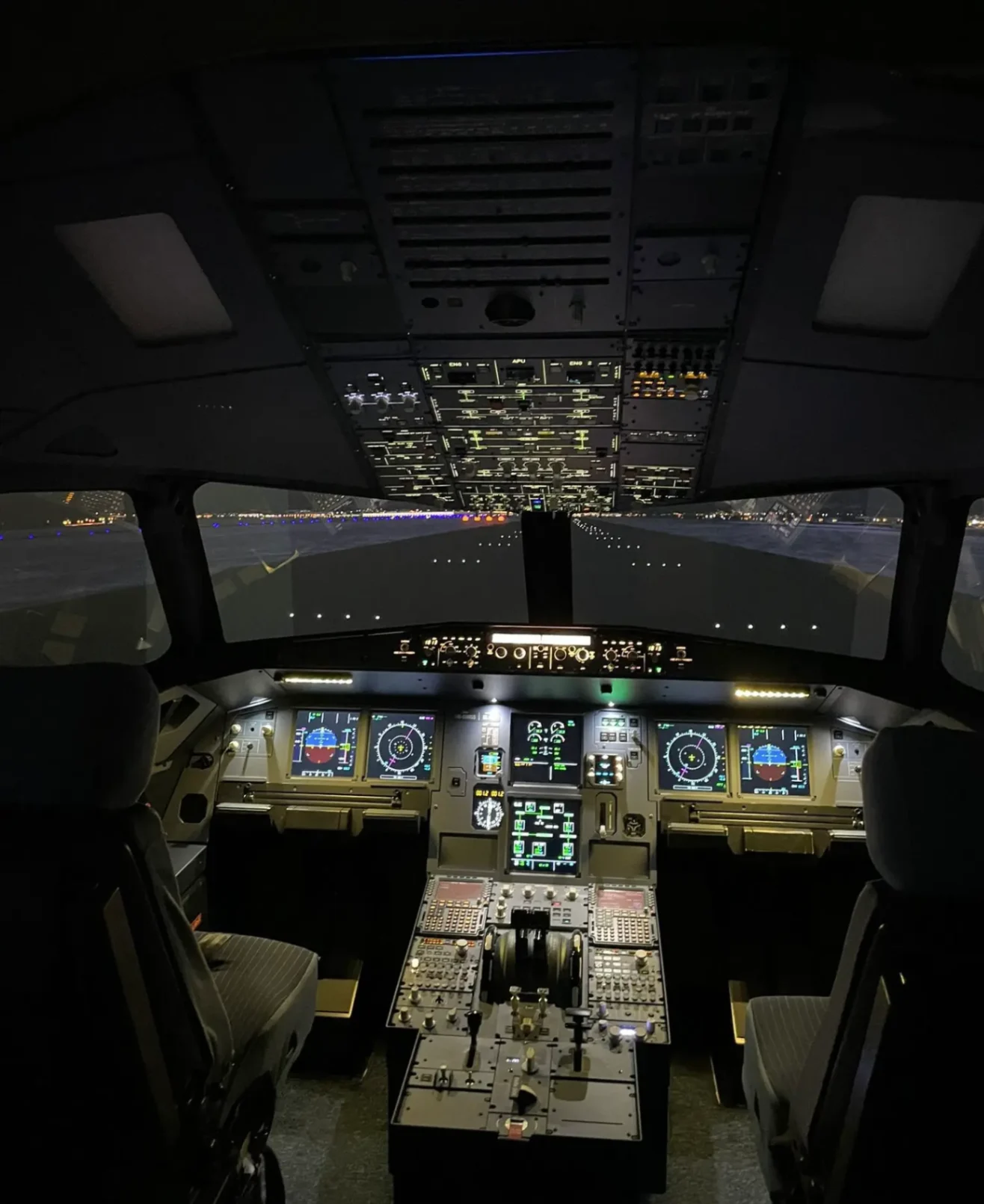 Cockpit complet d’un simulateur de vol Airbus A320 avec écrans de navigation allumés et vue de piste devant le pare-brise.