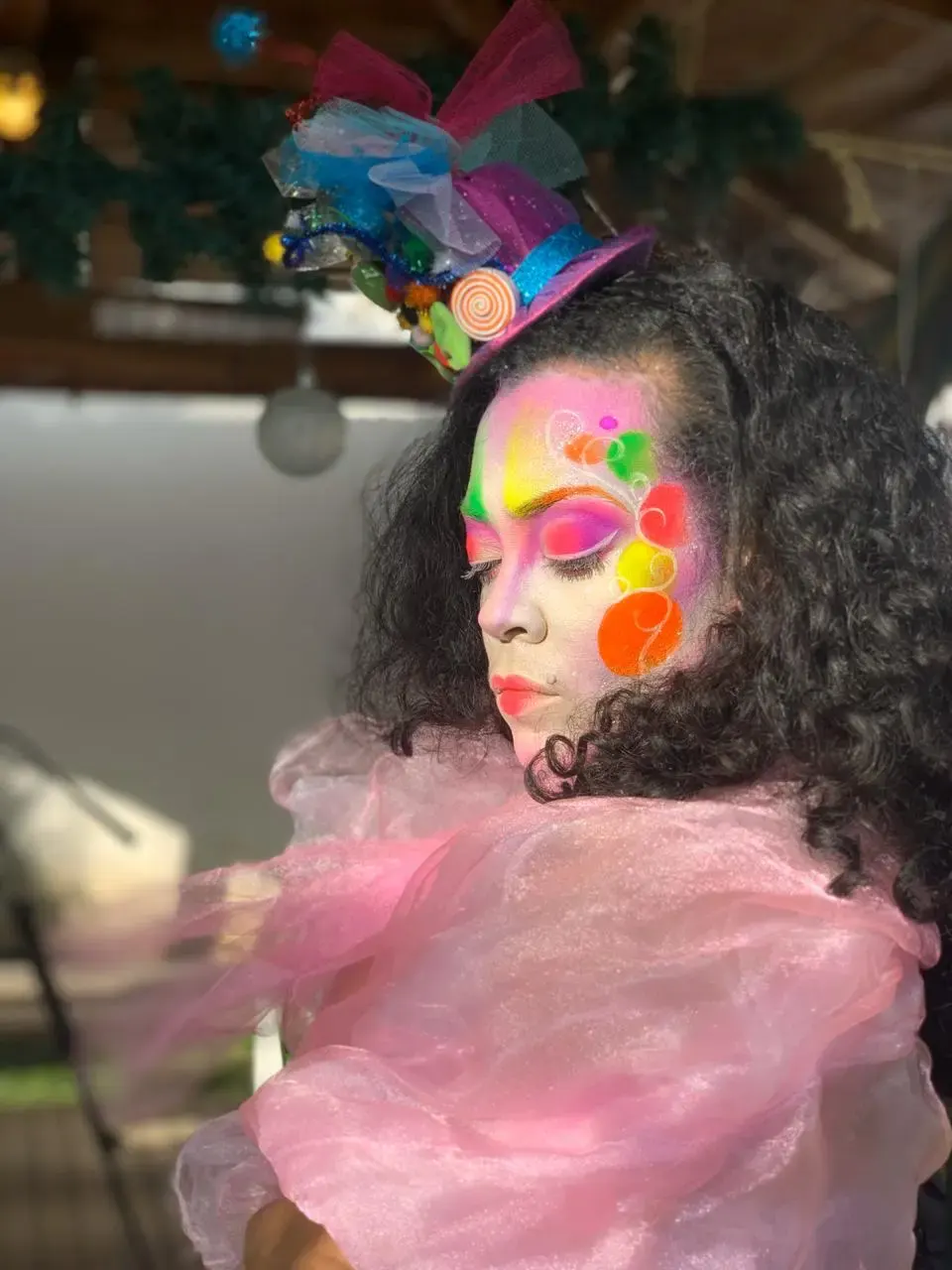 Femme avec un maquillage artistique très coloré et un chapeau décoratif, posant avec une tenue rose en tulle.