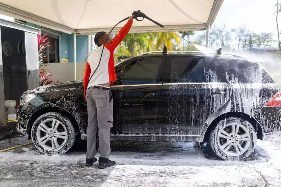 Professionnel lavant un SUV noir à la mousse avec un nettoyeur haute pression.