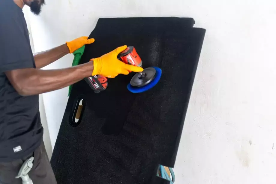 Technicien nettoyant un panneau de voiture avec une polisseuse et des gants orange.
