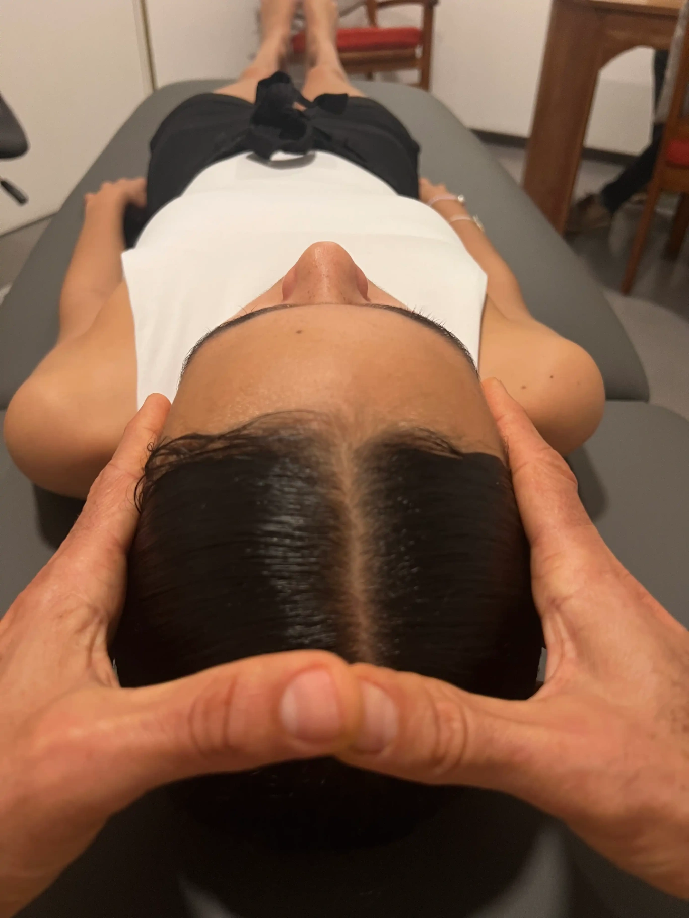 Séance d’ostéopathie crânienne sur une femme allongée, praticien posant délicatement ses mains sur son crâne.