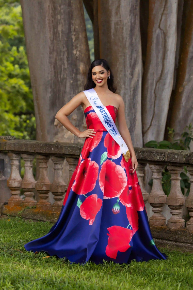Candidate Miss Martinique 2025 posant en robe longue bleue à fleurs rouges dans un jardin tropical