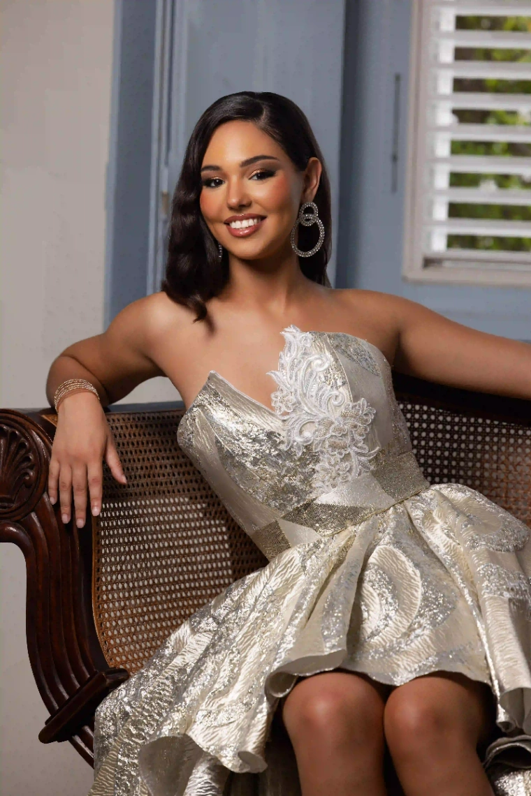 Portrait d’une candidate Miss Martinique 2025 assise dans un fauteuil, portant une élégante robe dorée.