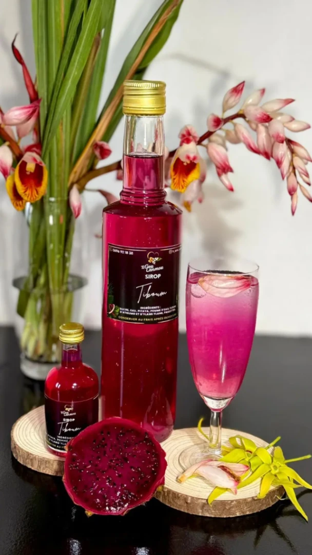 Bouteille de sirop Tiboum artisanale accompagnée d’un verre rafraîchissant à base de pitaya, présentée avec des fleurs exotiques