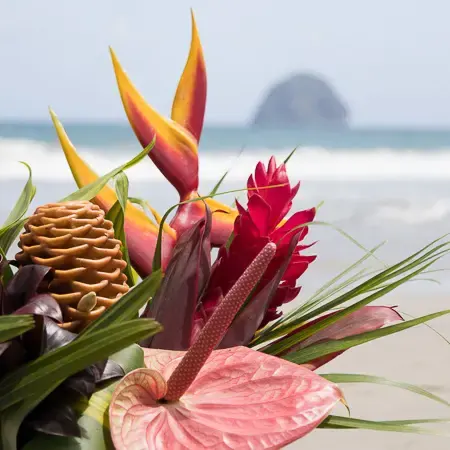 Composition florale tropicale avec anthurium rose et fleurs exotiques, en arrière-plan une plage et la mer.