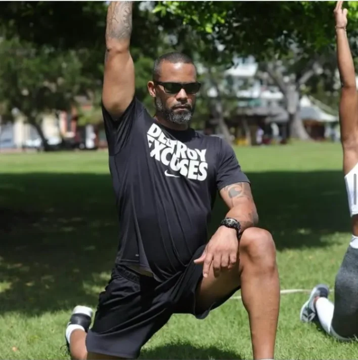 Coach sportif réalisant un étirement en extérieur dans un parc