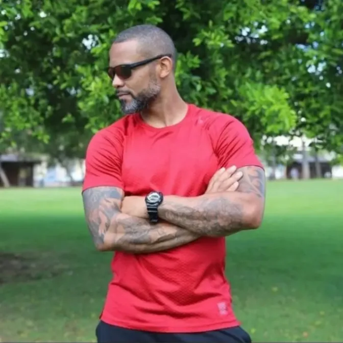 Coach sportif bras croisés portant un t-shirt rouge dans un parc