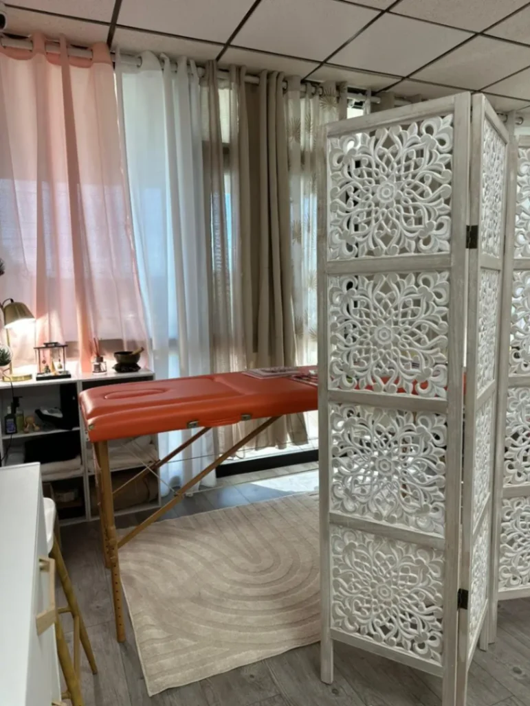 Cabine de massage chaleureuse avec table de soins, paravent décoratif et ambiance bien-être apaisante.