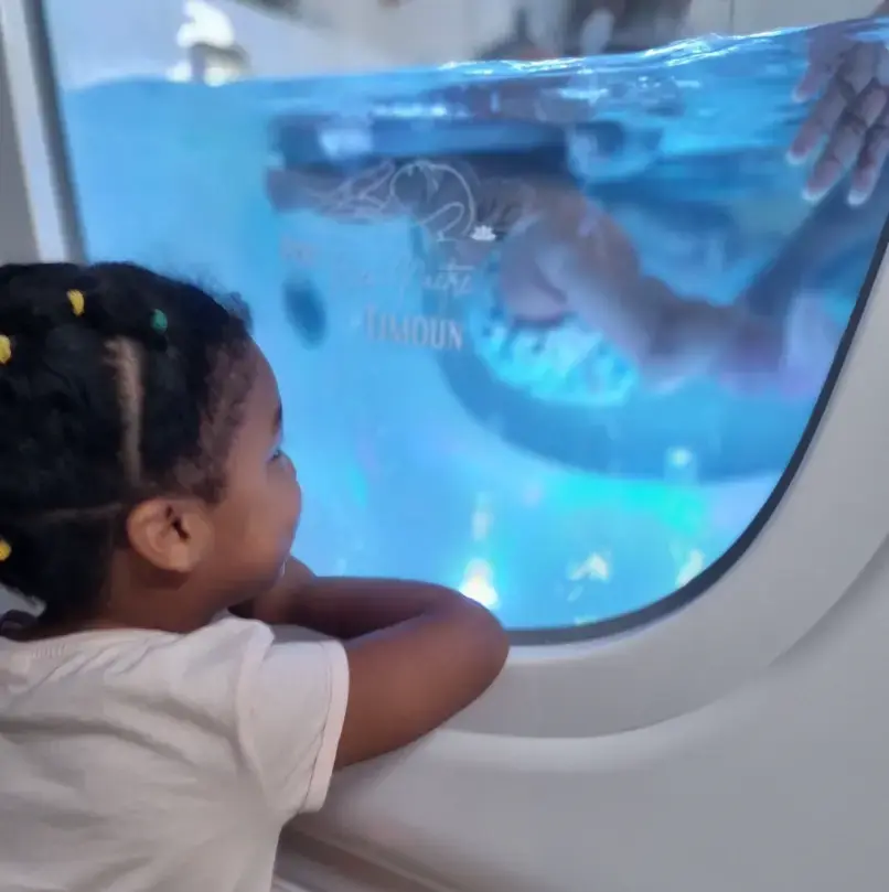 Jeune enfant observant un bébé dans un bassin de spa à travers une vitre, dans un espace bien-être.