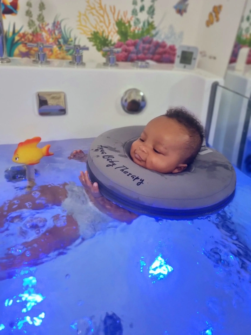 Bébé détendu flottant dans un bain de spa grâce à un coussin de flottaison, lors d’une séance d’hydrothérapie.