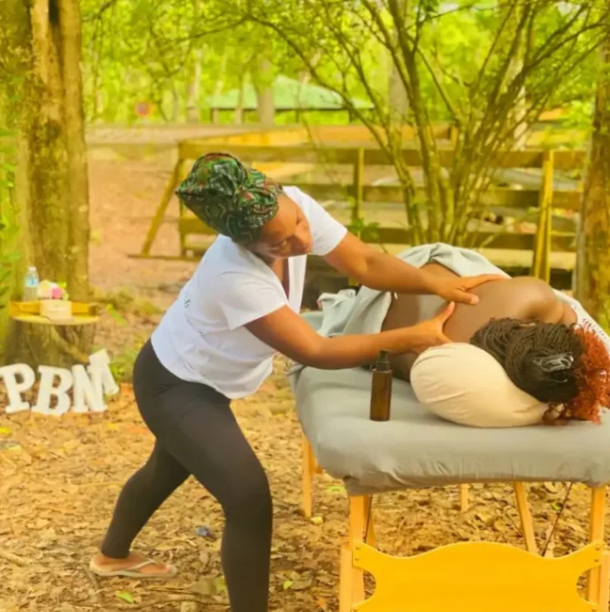 Praticienne réalisant un massage bien-être sur une table de massage en pleine nature, dans un cadre boisé et apaisant.