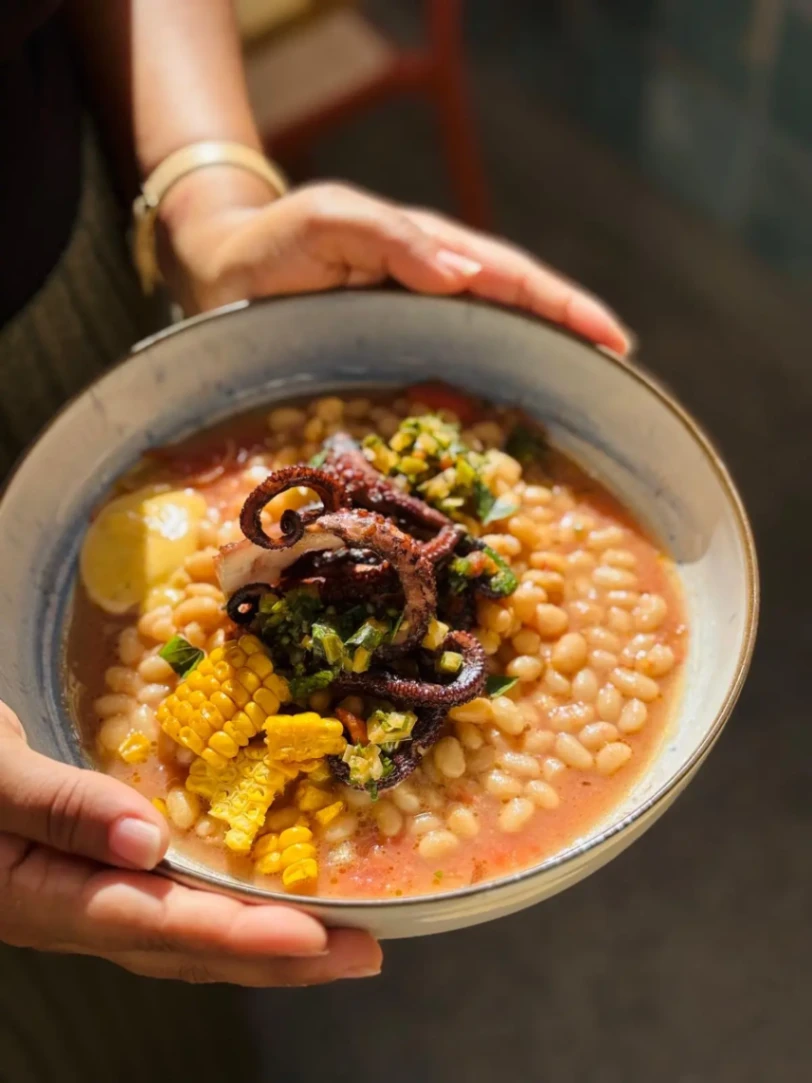 Bol de ragoût de haricots blancs garni de poulpe grillé et de maïs dans un bouillon parfumé