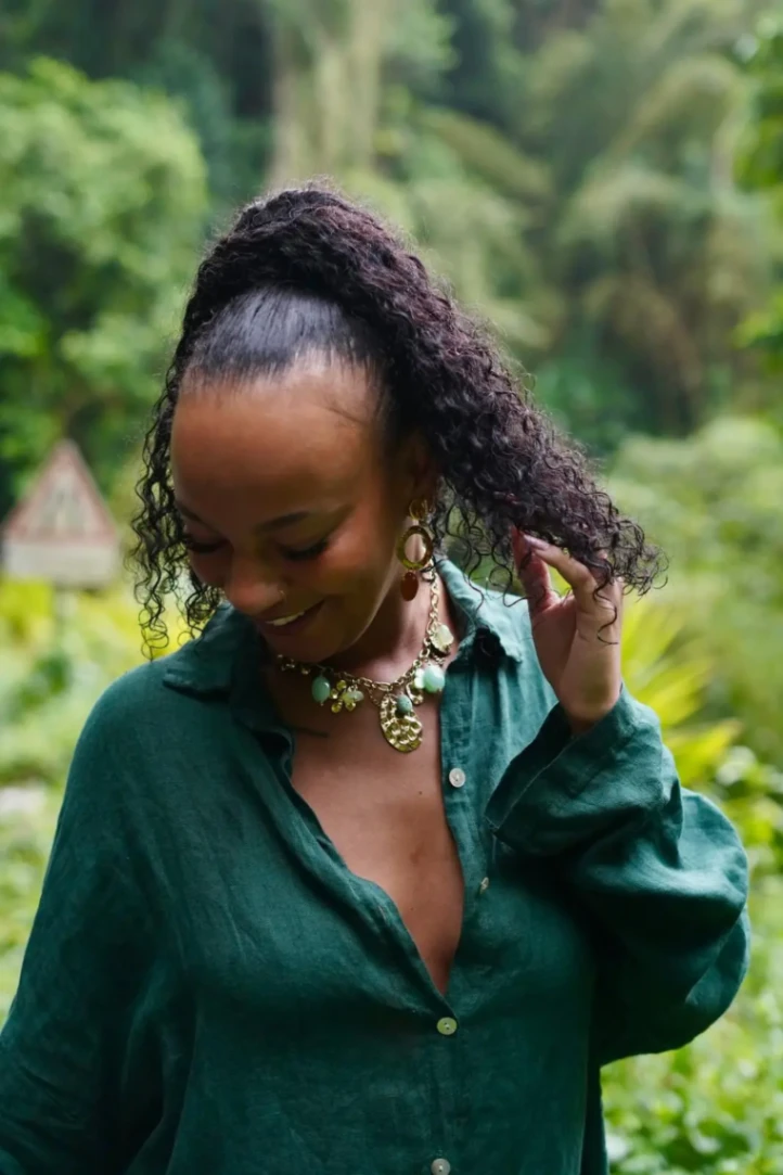 Femme portant un collier et des boucles d’oreilles dans un environnement naturel tropical.