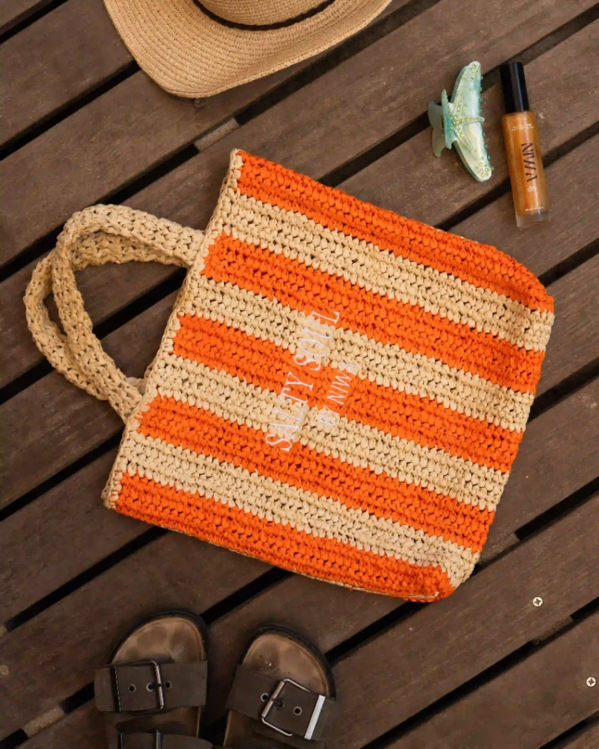 Sac de plage rayé orange et beige accompagné d’un soin NIWA et d’accessoires estivaux.