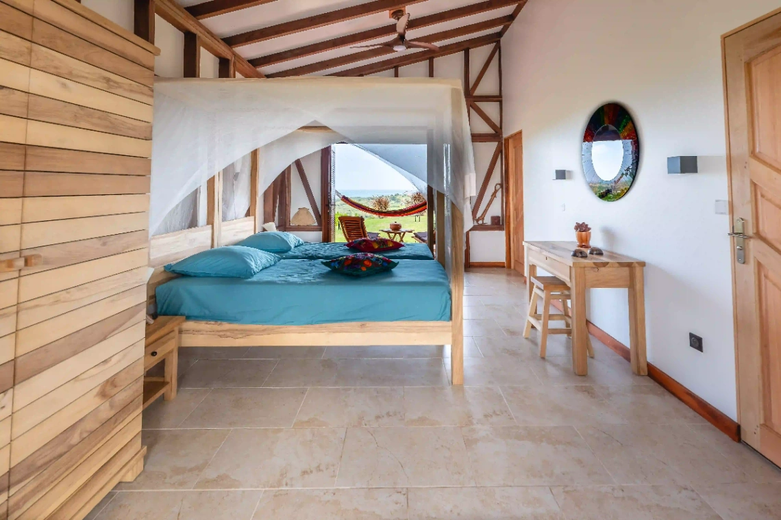 Chambre spacieuse avec lit à baldaquin, mobilier en bois et vue sur la nature en Martinique.